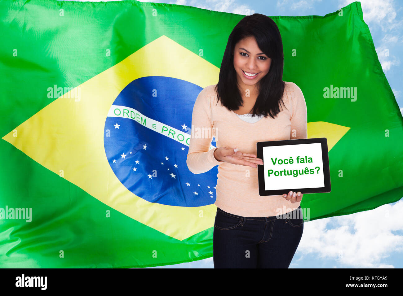Jeune femme tenant la tablette numérique demander parlez-vous portugais devant le drapeau brésilien Banque D'Images