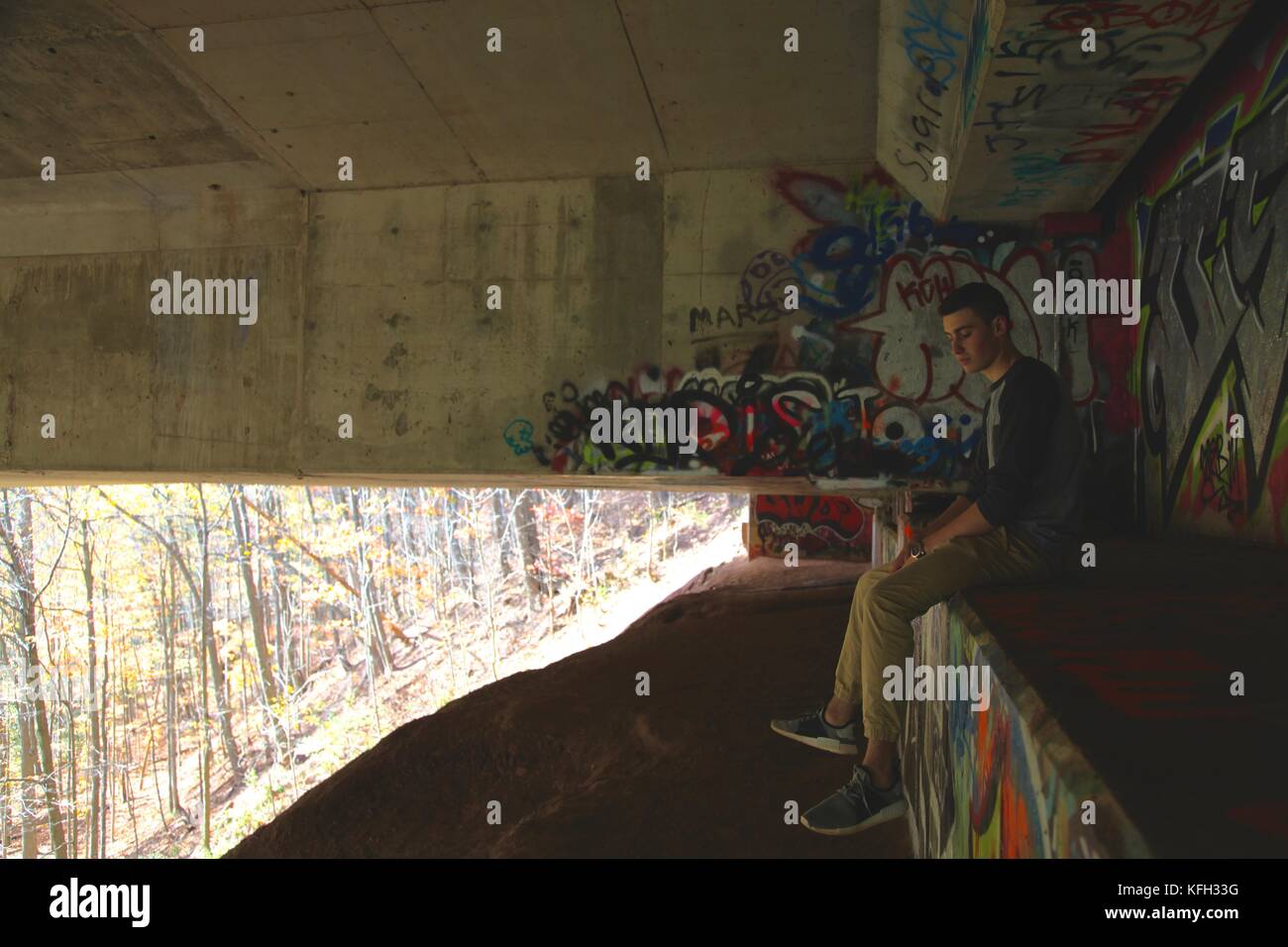 Adolescent assis sous un pont abandonné plein de graffitis Banque D'Images
