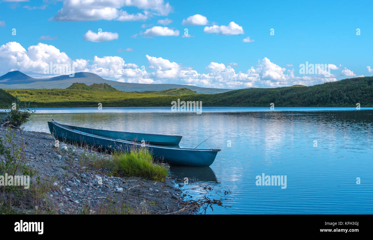 Deux canoës bleu sur le bord d'un lac calme avec de vertes collines en arrière-plan Banque D'Images