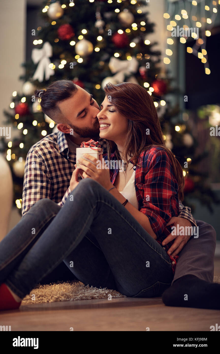 Les jeunes époux hugging et embrasse sa femme pendant que donne son cadeau de Noël Banque D'Images