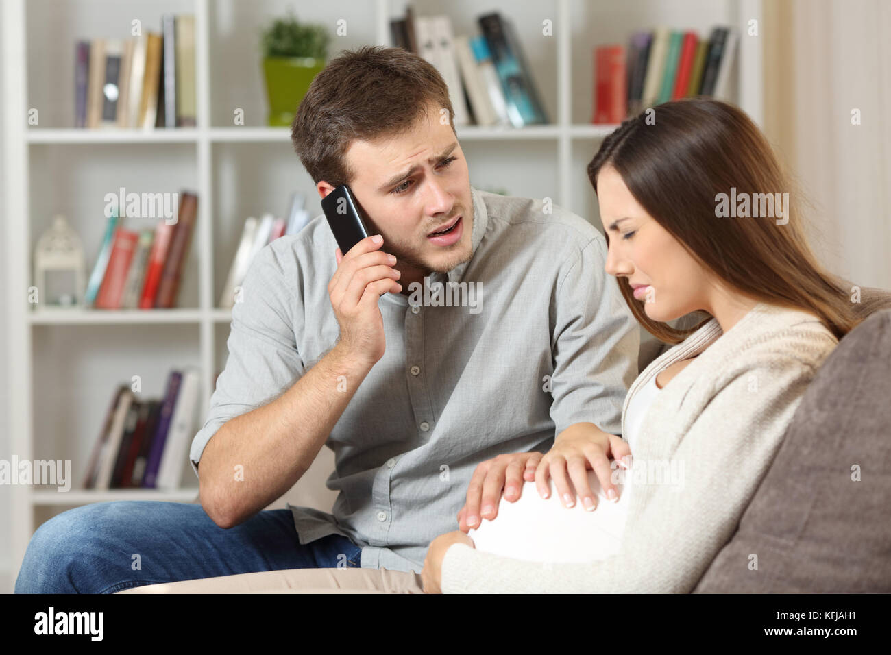 Femme enceinte souffrant et mari appelant à médecin assis sur un canapé à la maison Banque D'Images