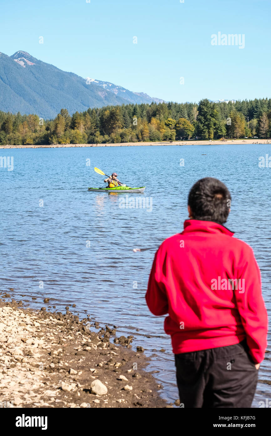 Un garçon asiatique en molleton rouge ressemble à un kayakiste dans le calme de l'eau du lac journée ensoleillée d'automne Banque D'Images