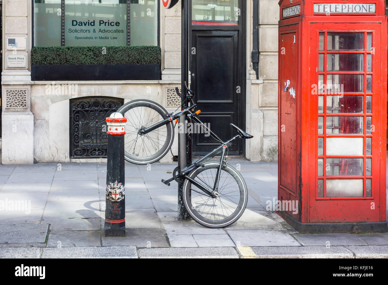 En stationnement vélo sécurisé verrouillé à un bollard post à côté d'un téléphone rouge fort, Ville de London, UK Banque D'Images