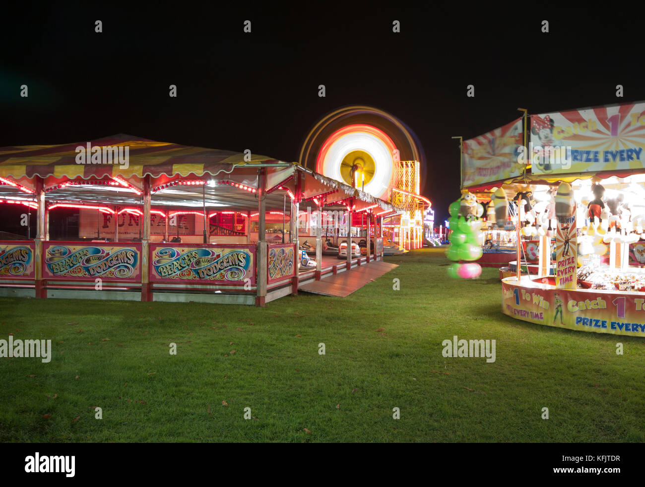 Voyageant de nuit fête foraine avec des lumières brillantes expositions éclairées avec grande roue de Ferris UK Banque D'Images