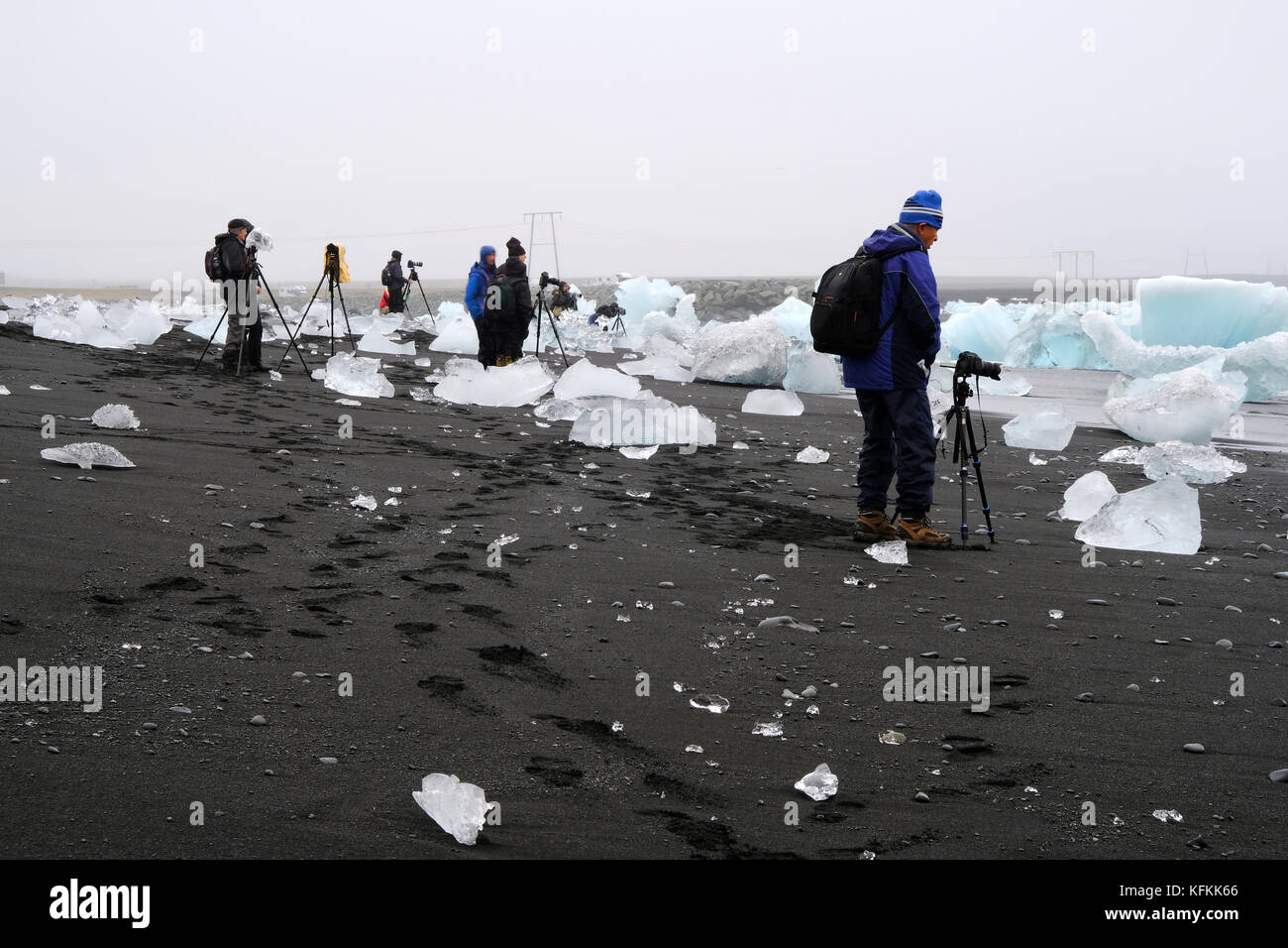 Les photographes en tournée photo avec des appareils photo et des trépieds debout et photographiant des icebergs se sont délassés sur la plage de sable noir de diamants à Jokulsarlon Islande Banque D'Images