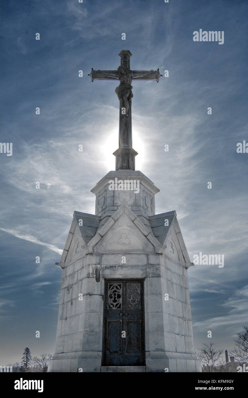 La lumière du soleil brumeux de l'été un crucifix bronze halos au sommet d'un tombeau en marbre. Banque D'Images La lumière du soleil brumeux de l'été un crucifix bronze halos au sommet d'un tombeau en marbre. Banque D'Images
