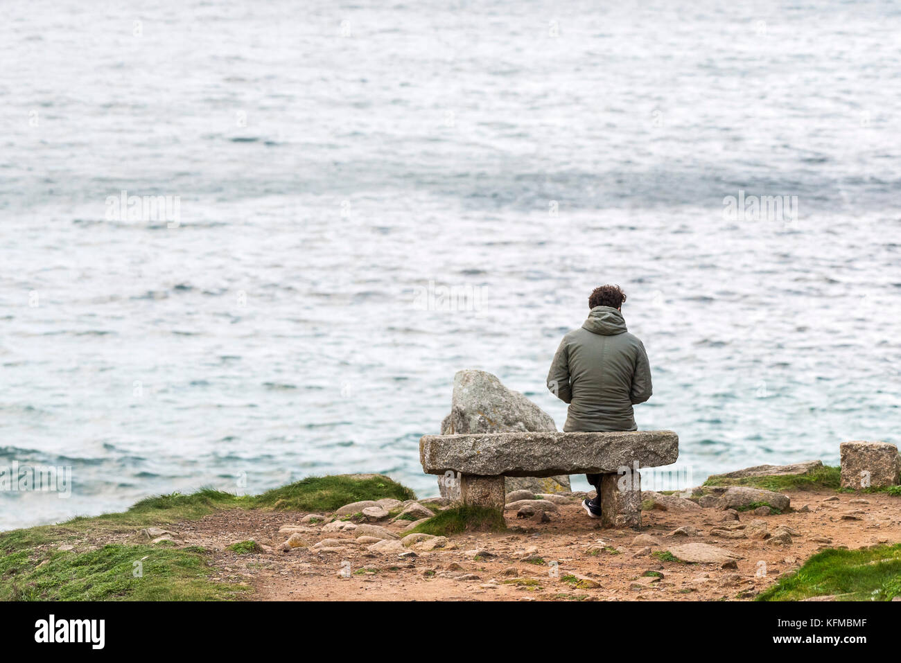 Porth Nanven Cornwall - un homme solitaire assis sur un siège en granit surplombant Porth Nanven, dans les Cornouailles. Banque D'Images