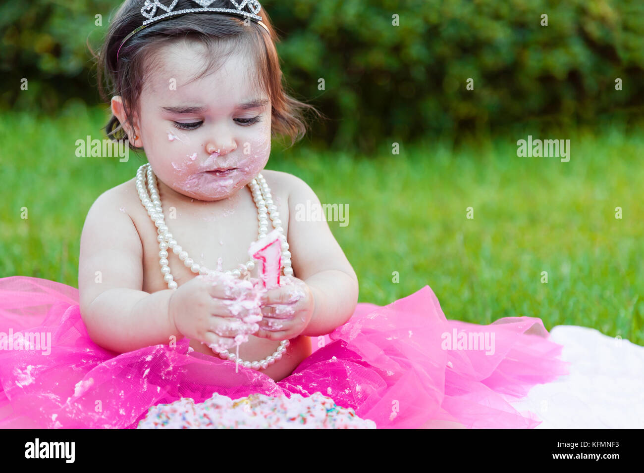Bébé fille bébé premier anniversaire anniversaire parti, jouant avec la bougie, sale visage et faire un gâchis de gâteau rose avec bougie. princess costume Banque D'Images