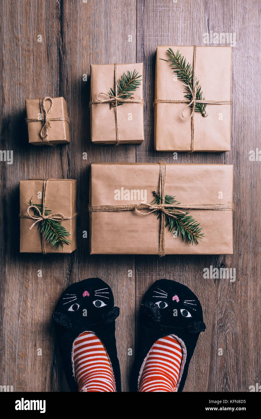 Pieds avec des chaussettes d'hiver chaud et chaussons chat debout devant des cadeaux de Noël. vue d'en haut. Banque D'Images