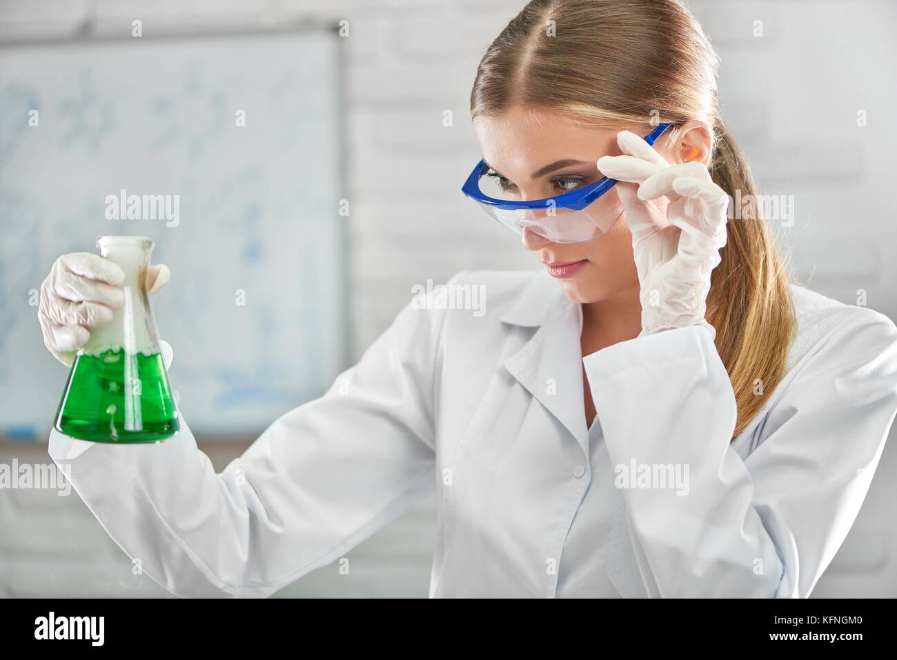 Close up d'une belle jeune femme portant des lunettes de protection scientifique examinant des échantillons de produits chimiques liquides dans une fiole de recherche expérience de laboratoire Banque D'Images