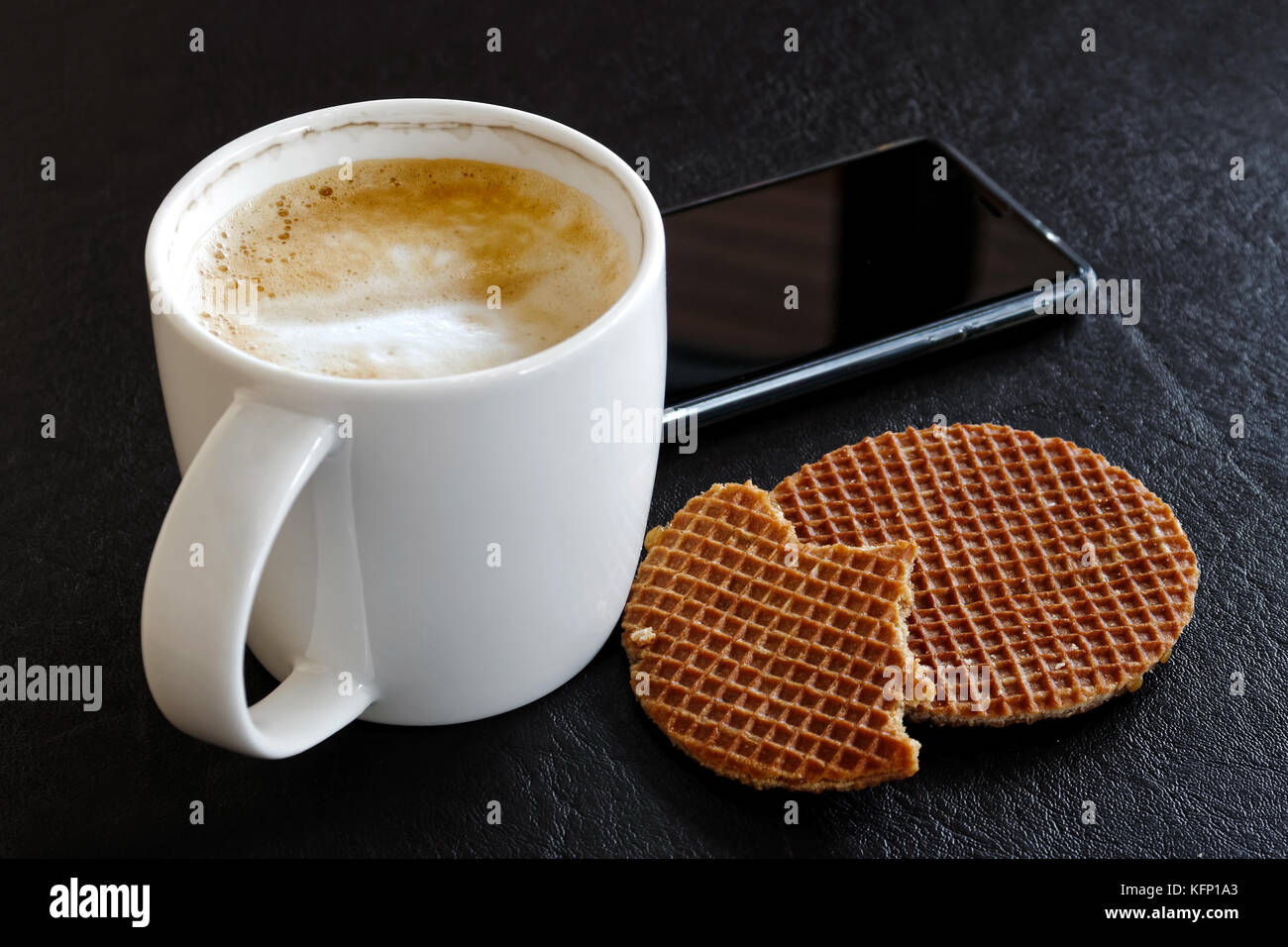 Délicieuse en blanc laiteux chope ivre à côté partiellement partiellement mangés waffle biscuits isolated on black. Banque D'Images