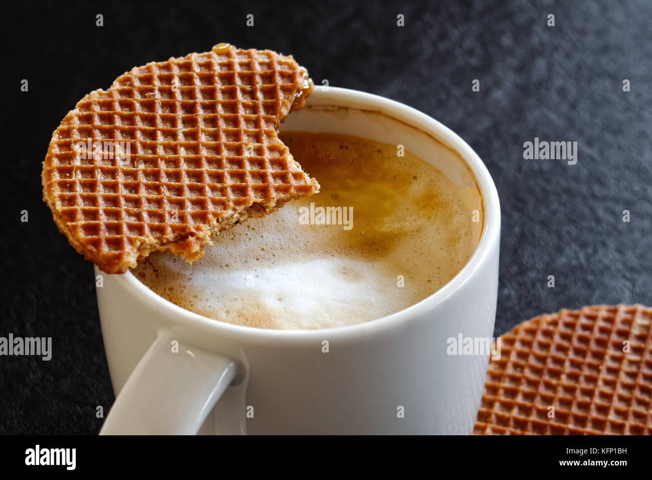 Détail de mug blanc laiteux avec délicieuse partiellement ivre et partiellement mangés un biscuit gaufre sur le dessus. fond noir. Banque D'Images