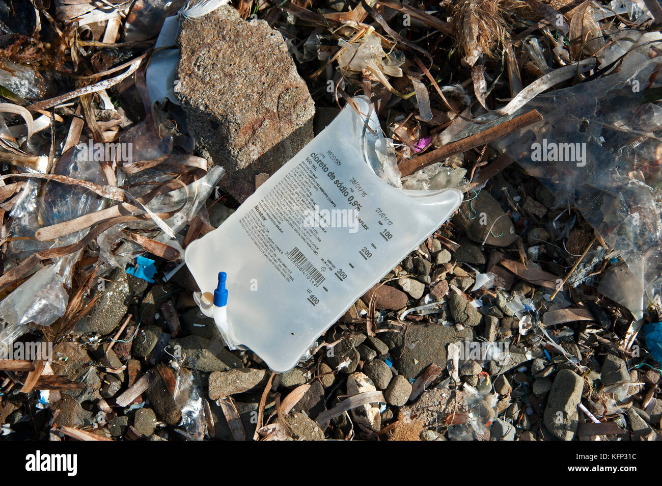 Un hôpital médical sac goutte salée rejetés intacts avec d'autres éléments plastiques sur une plage de galets à Minorque espagne Banque D'Images