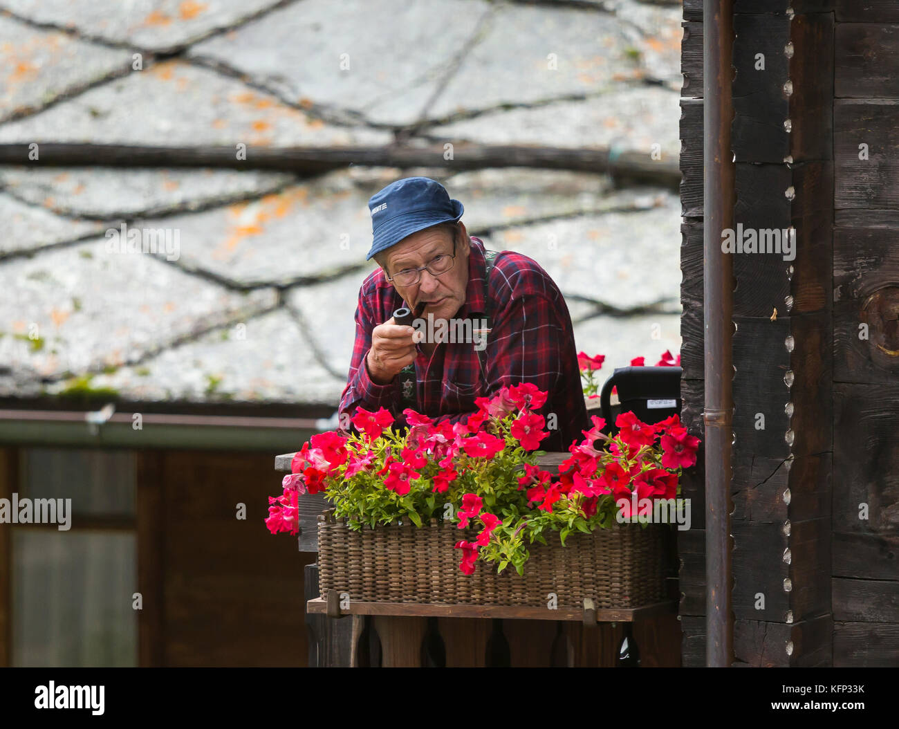 Herbriggen, Suisse - vieil homme fume sur balcon près de boite à fleurs. Banque D'Images