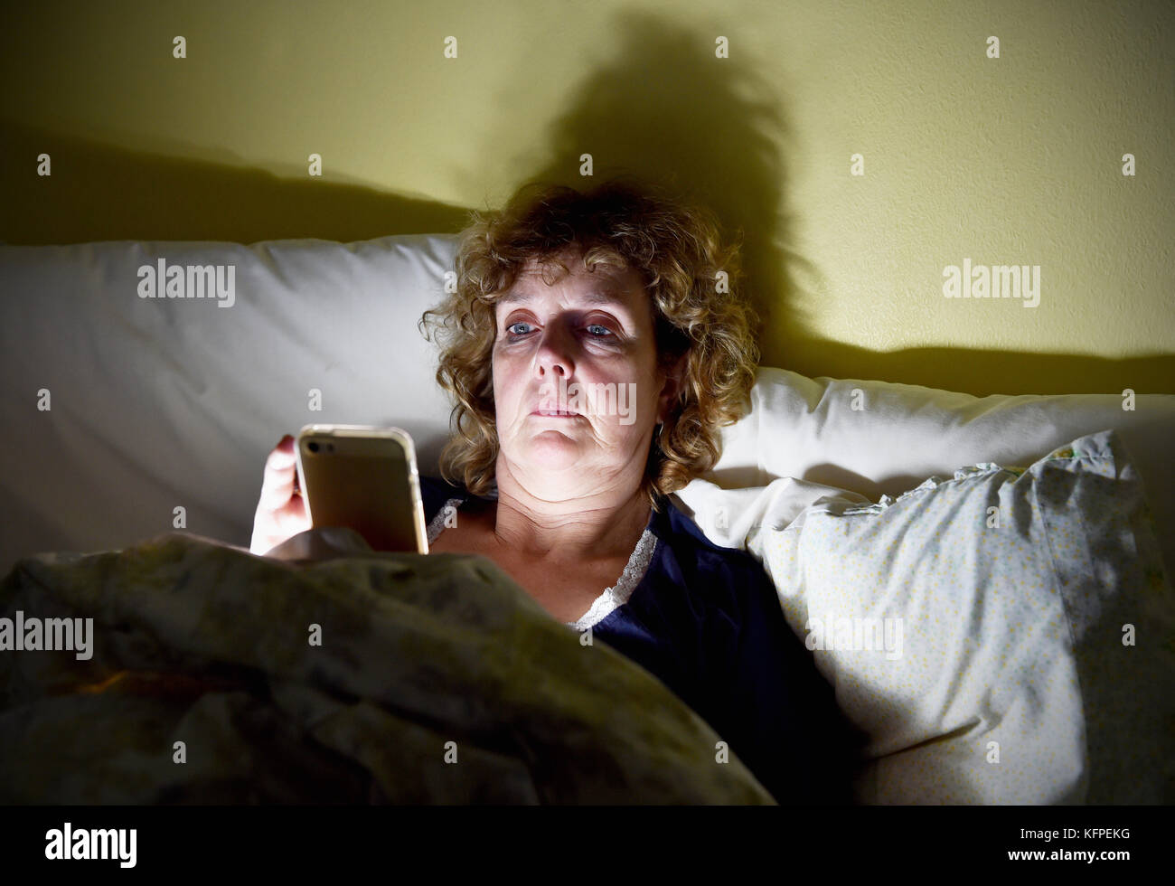 Femme d'âge moyen lisant son smartphone Apple iPhone au lit la nuit Banque D'Images