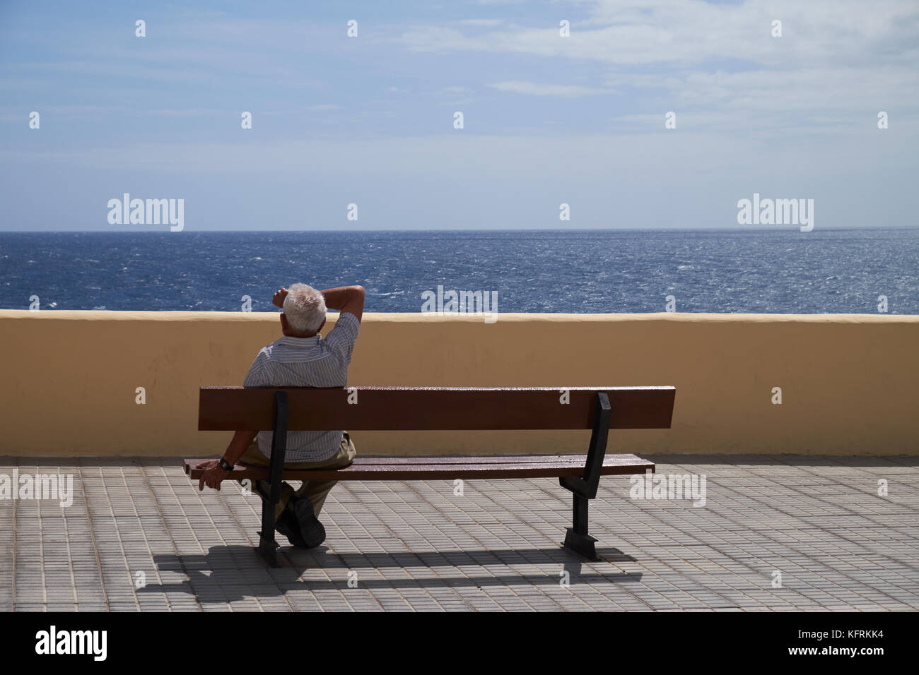 Vieil homme assis sur un banc en bord de mer. Los Abrigos, Granadilla de Abona, Tenerife, Canaries, Espagne. Banque D'Images
