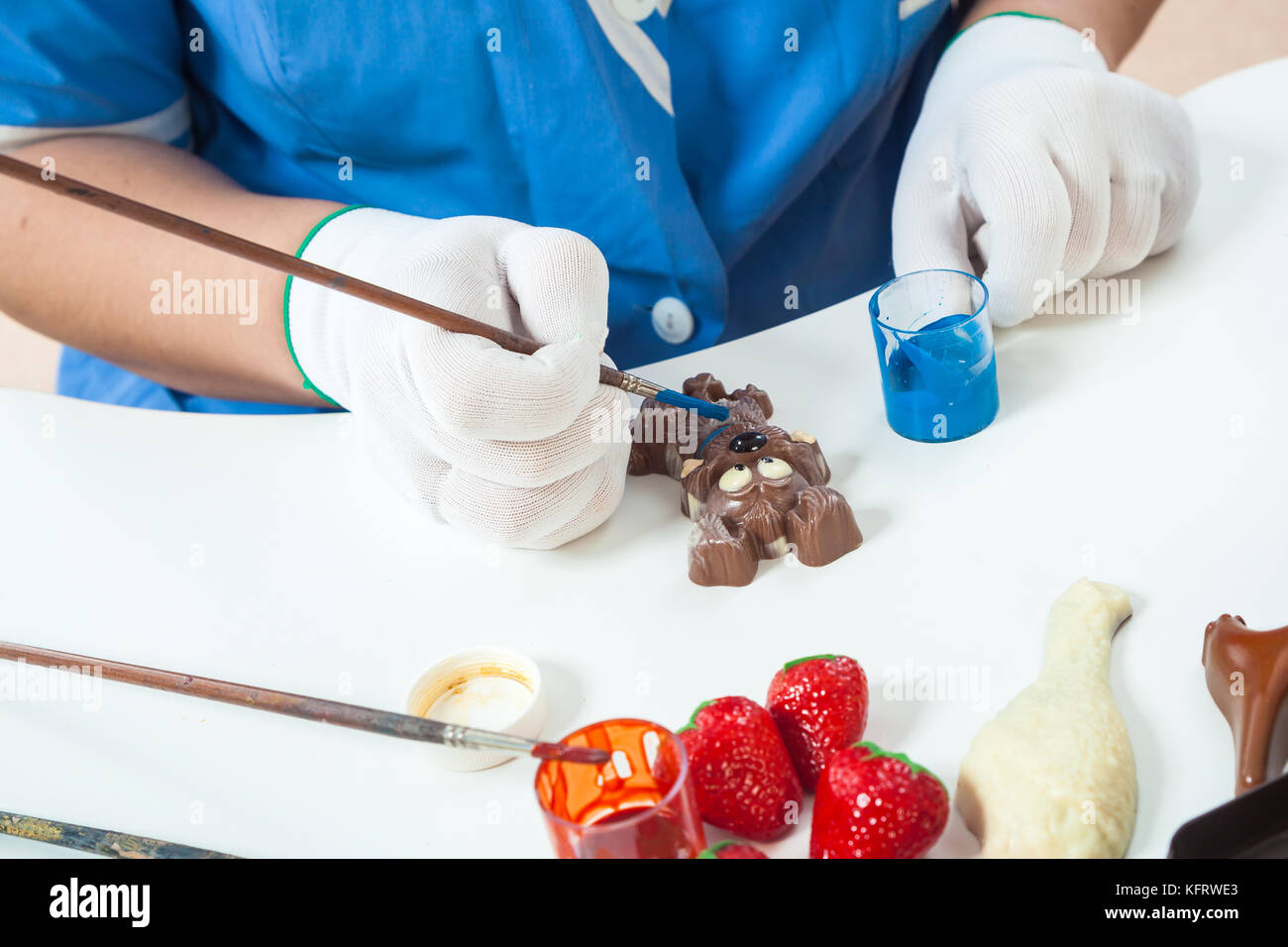 Une femme pâtissier avec l'uniforme bleu et blanc couleurs gants stériles en forme d'un chien de bonbons dans la couleur d'or avec peinture comestible sur un tableau blanc pour une nouvelle Banque D'Images