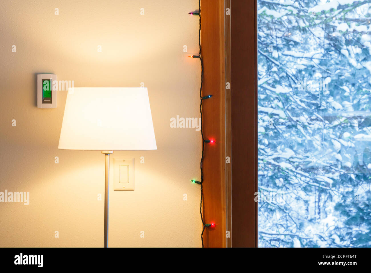 Accueil chaleureux salon intérieur avec thermostat électronique numérique, lampadaire, lumières de Noël et voir à travers les fenêtres de paysage de neige Banque D'Images