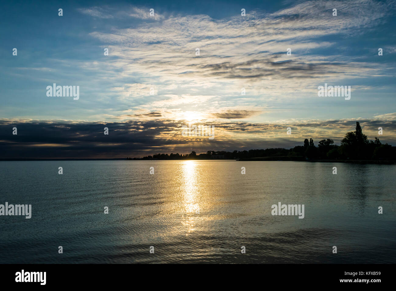 Beau lever de soleil sur le lac. Le soleil brille à travers les nuages de façon spectaculaire, silhouette d'arbres sur les rives du lac Balaton, en Hongrie. Banque D'Images
