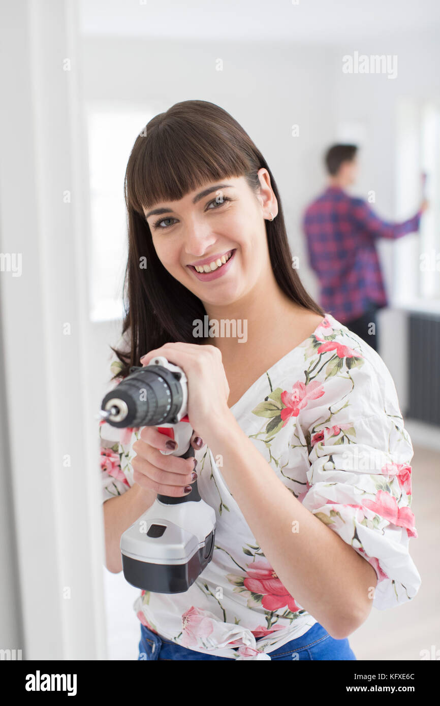 Femme à l'aide de la perceuse électrique comme couple rénovent des biens ensemble Banque D'Images