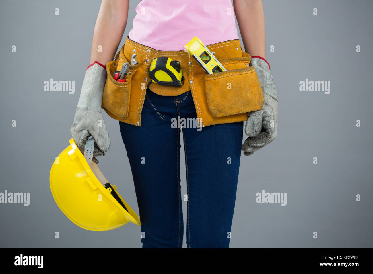 Section intermédiaire de femme avec ceinture d'outils et holding hard hat contre l'arrière-plan gris Banque D'Images