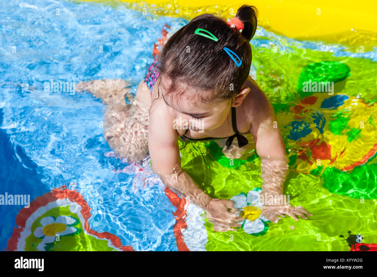 Mignon, heureux, souriant bébé fille en bas âge, nageant, et jouant dans la piscine gonflable colorée d'arrière-cour le jour chaud d'été. Treize mois Banque D'Images