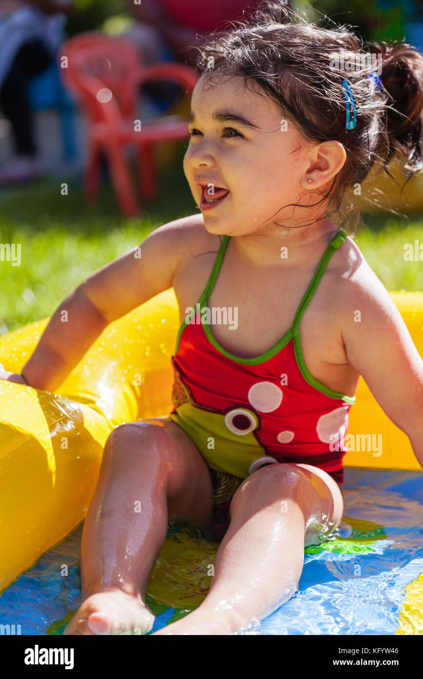 Mignon, heureux, souriant bébé fille en bas âge, jouant dans la piscine gonflable colorée de jardin d'arrière-cour dans la journée chaude d'été. Treize mois Banque D'Images