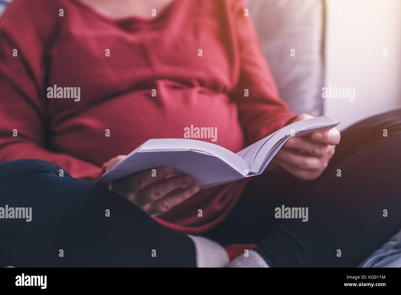 Pregnant woman reading livre sur la grossesse et la maternité dans la salle de séjour, selective focus Banque D'Images