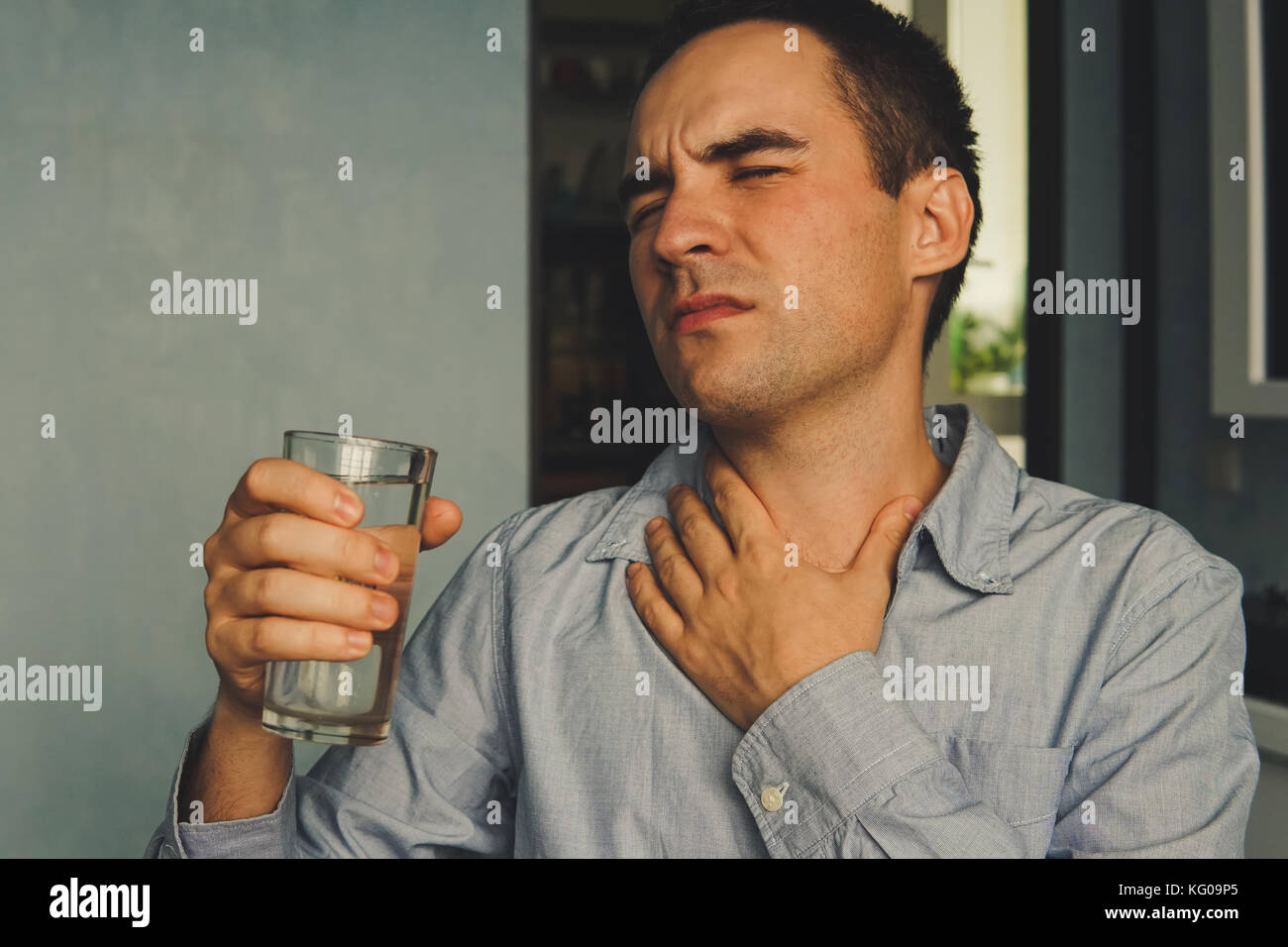 Une gorge desséchée et un verre d'eau dans la main. beau mec dans des vêtements décontractés tient un verre d'eau et de toucher sa gorge alors qu'il était assis sur le cou Banque D'Images