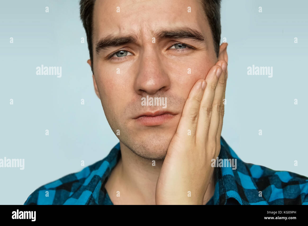 Un jeune mec avec une triste émotion sur son visage maintenant sa main sur la mâchoire du patient sur un fond bleu. portrait d'un homme dans l'expression douloureuse avec Banque D'Images