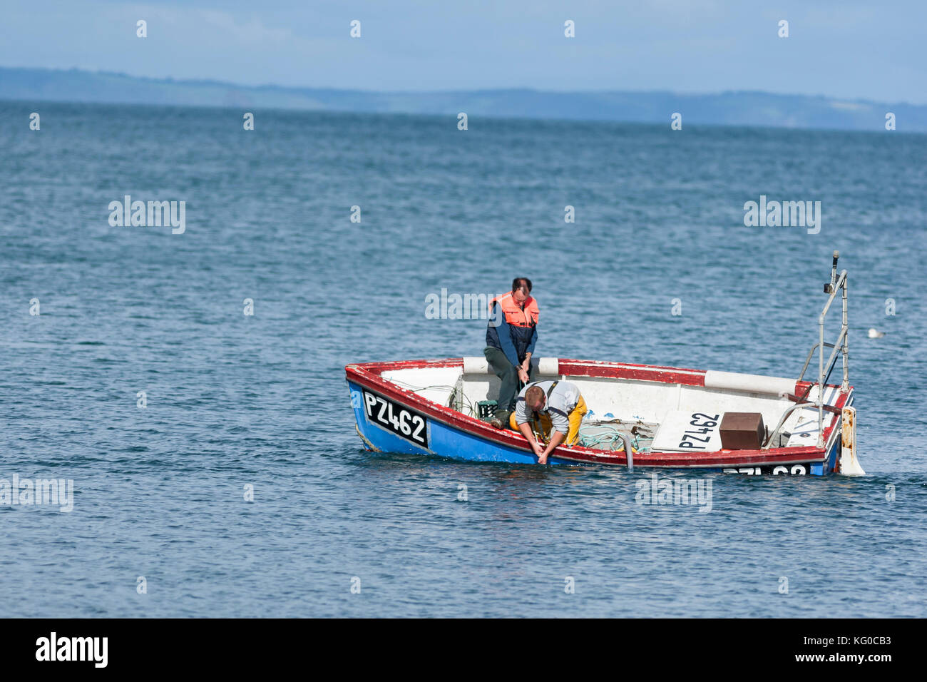 Les hommes tirant sur coincé lobster pot corde près de chavirement bateau de pêche traditionnel Cornwall UK Banque D'Images