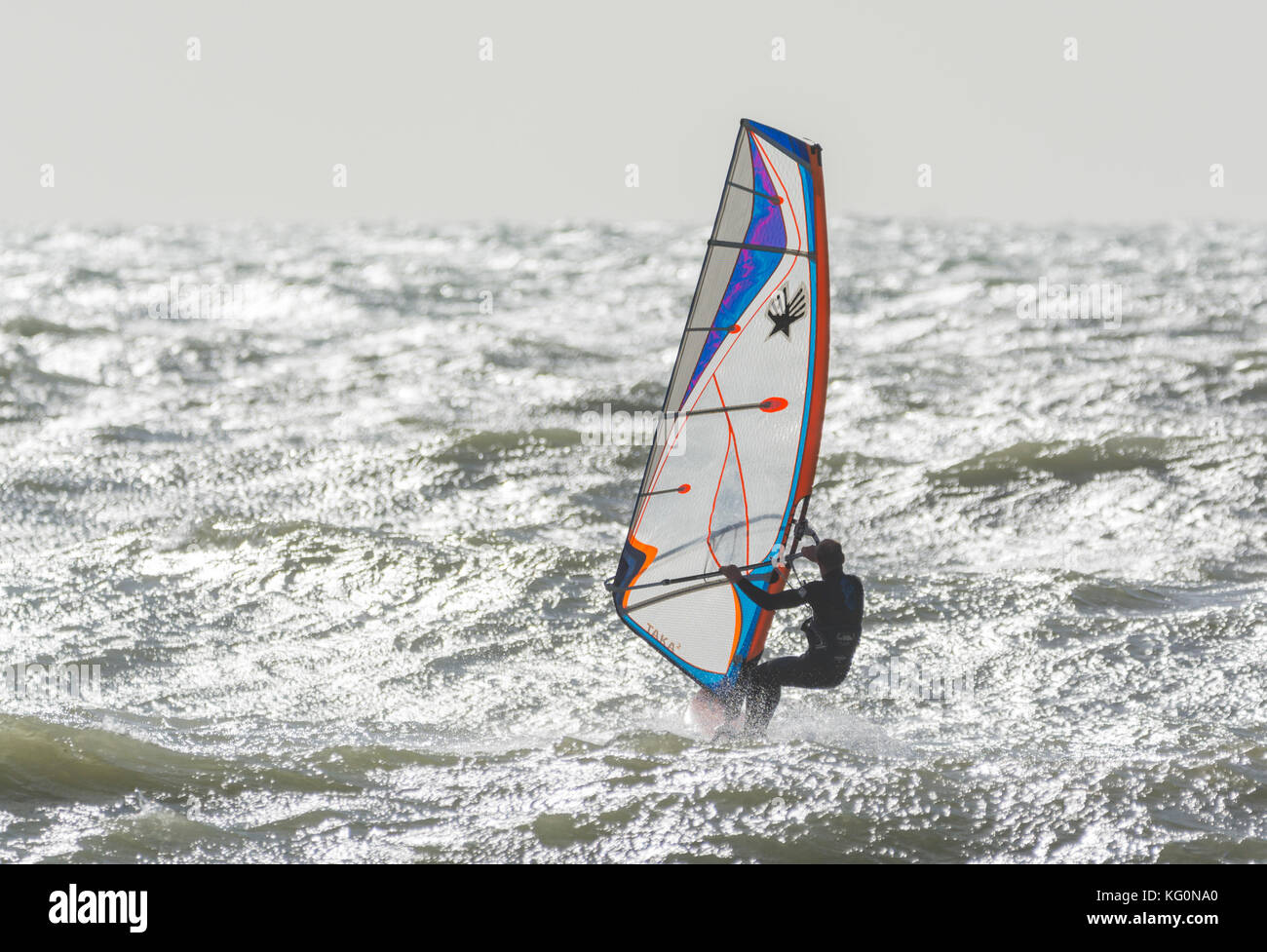 Windsurfer en mer par un jour de vent avec soleil reflétant dans l'eau. Banque D'Images