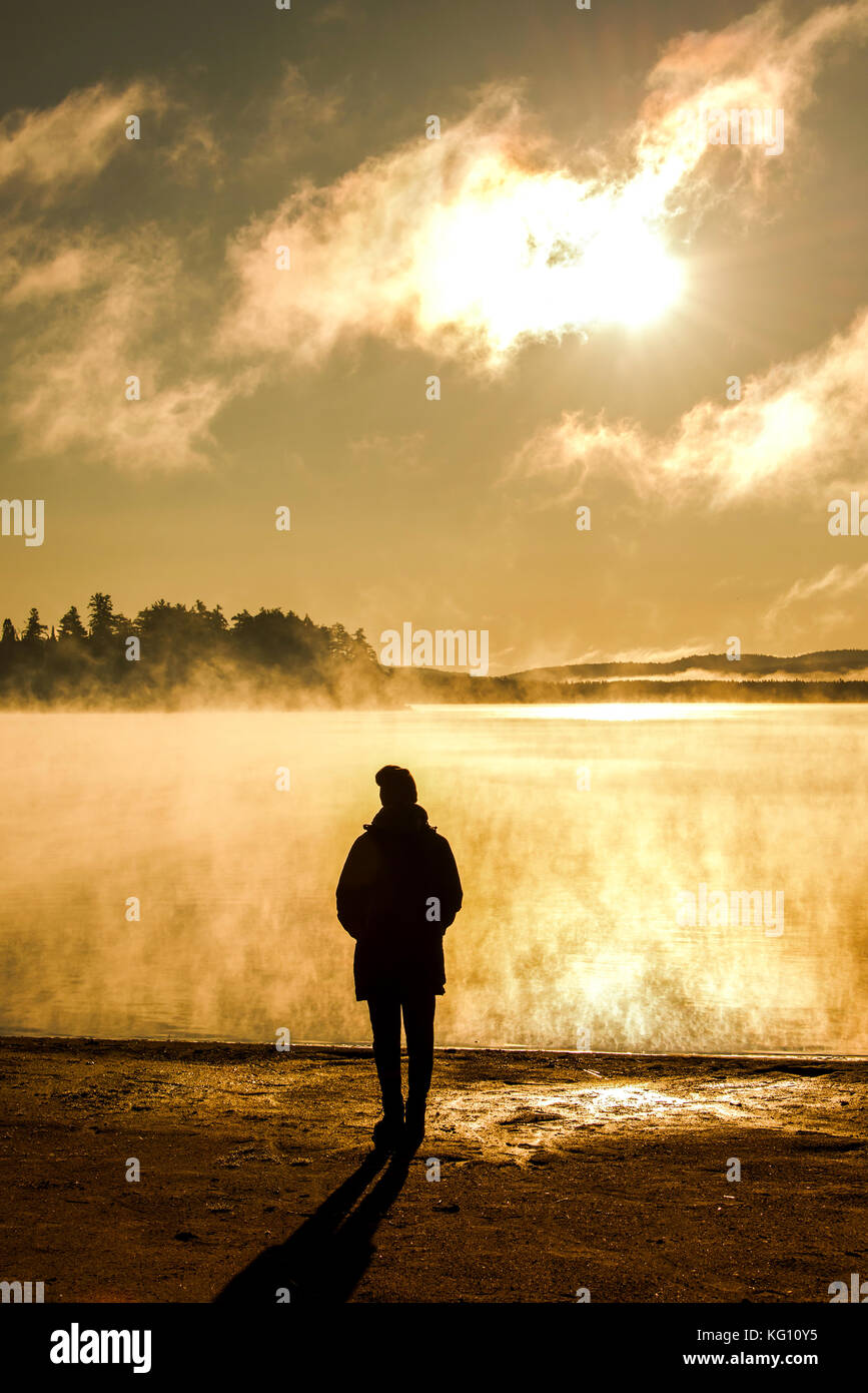 Belle femme debout au lac des deux rivières en algonquin parc national au Canada regarder le lever du soleil avec la brume dans la brume du lac nimbé d'swamp Banque D'Images