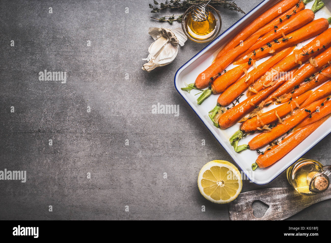 Bébé carottes rôties garnie sur une plaque de cuisson avec le thym, le miel, l'ail et citron sur fond de béton gris, vue du dessus, les légumes-racines en bonne santé. Banque D'Images