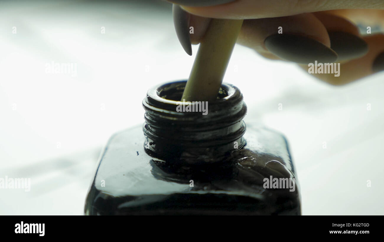 Main femelle dunks brosse dans un pot d'encre pour dessiner de près. Pinceaux chinois à l'ancienne avec mise au point sélective. Détail d'un pinceau chinois tout en dessinant une ligne en arrière-plan clair Banque D'Images