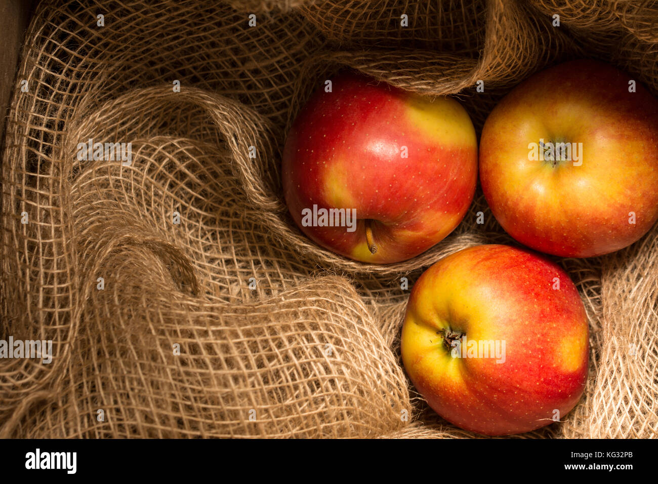 Trois mûres, les pommes rouges et jaunes stockés sur un filet de jute Banque D'Images