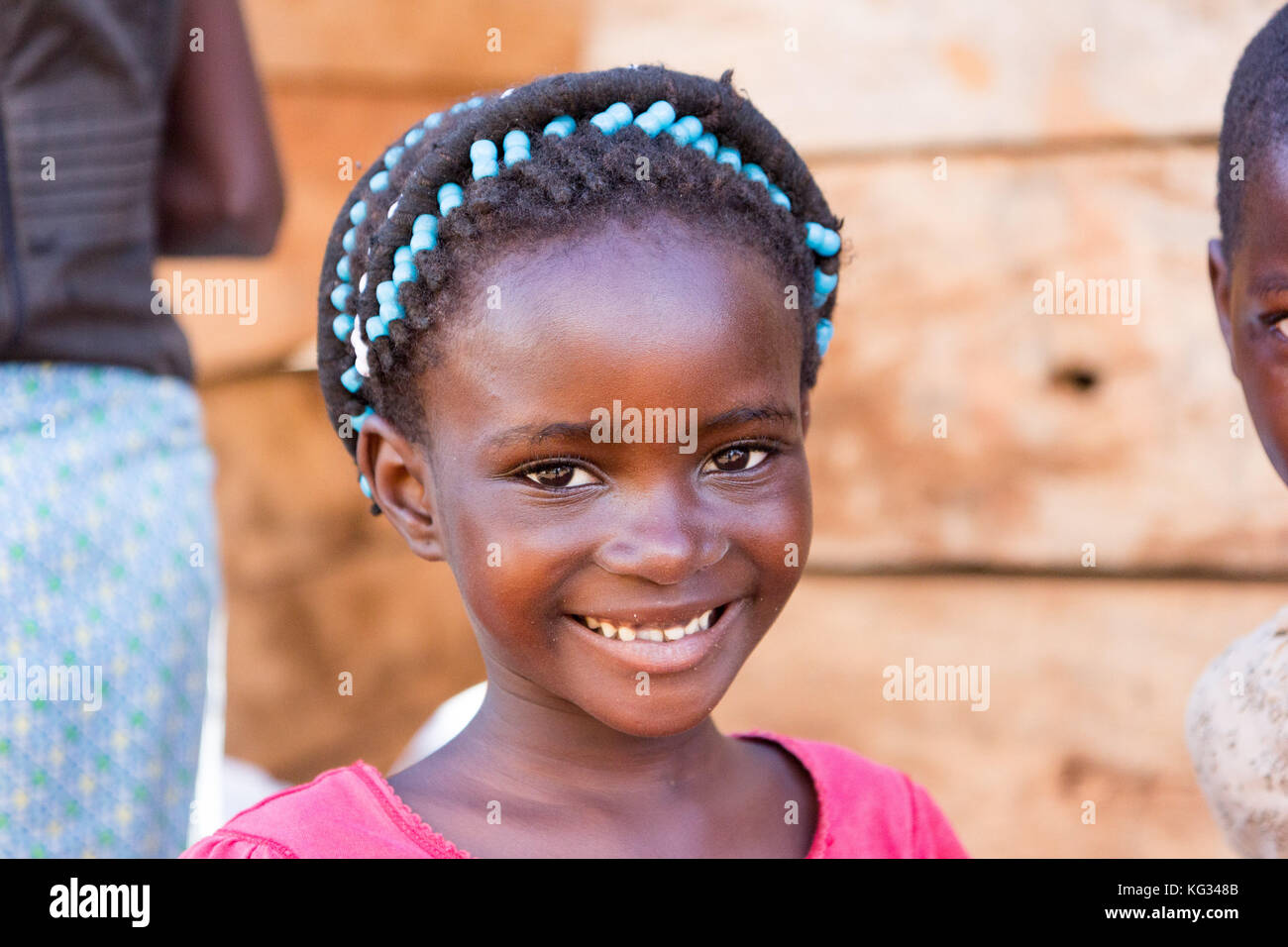 Une jeune fille souriante avec perles colorées sur ses tresses, elle est posant devant une cabane en bois. Banque D'Images
