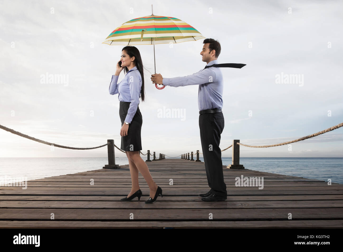 Businessman holding umbrella pour femme sur boardwalk over sea Banque D'Images