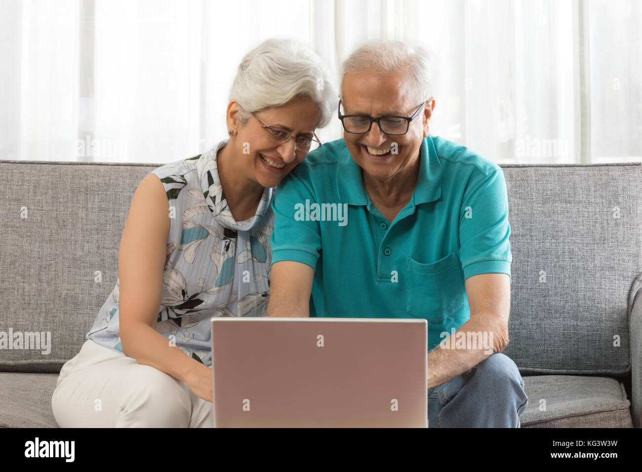 Couple using laptop sitting on sofa Banque D'Images