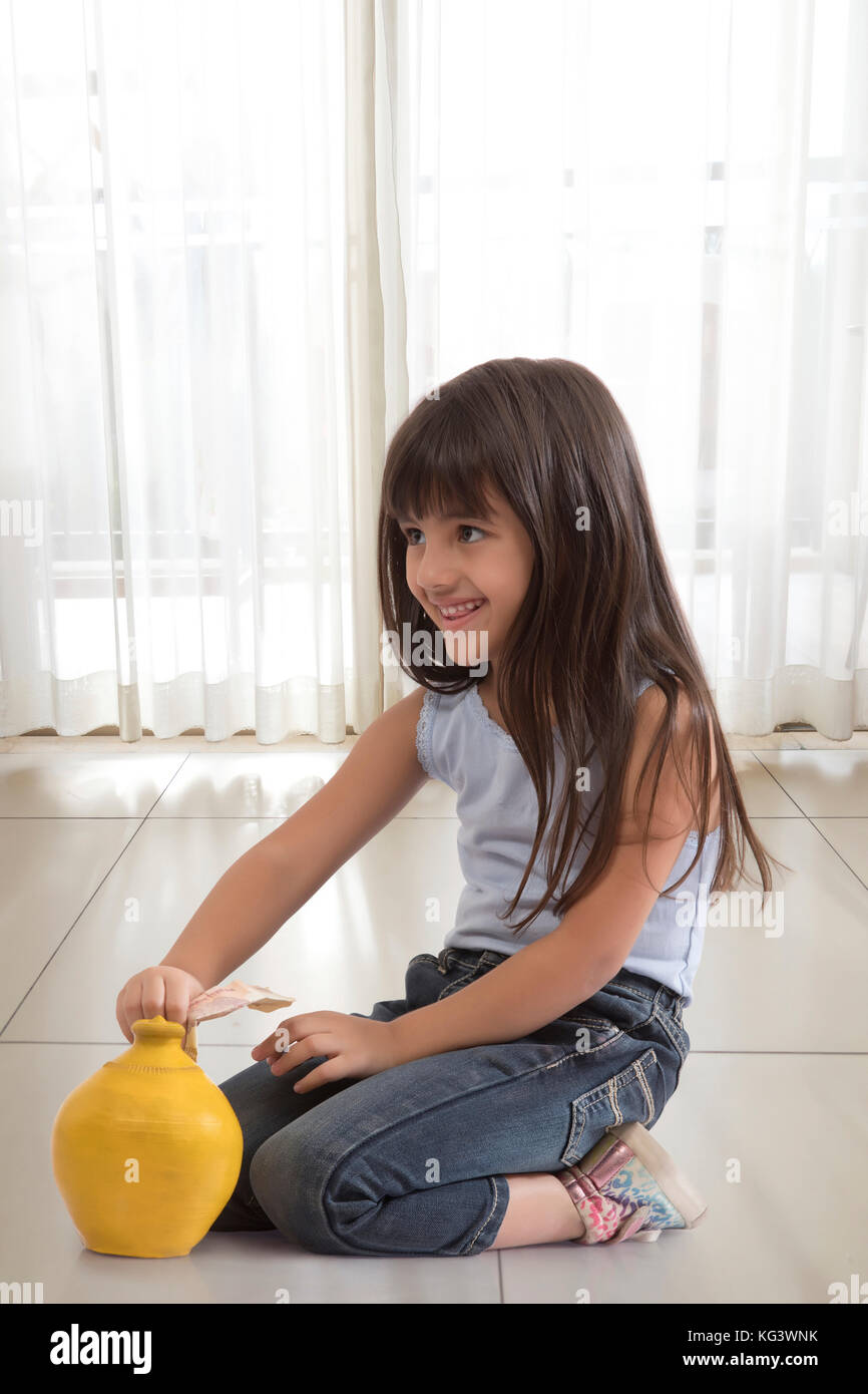 Petite fille assise sur le plancher et mettre de l'argile en billets de banque tirelire Banque D'Images