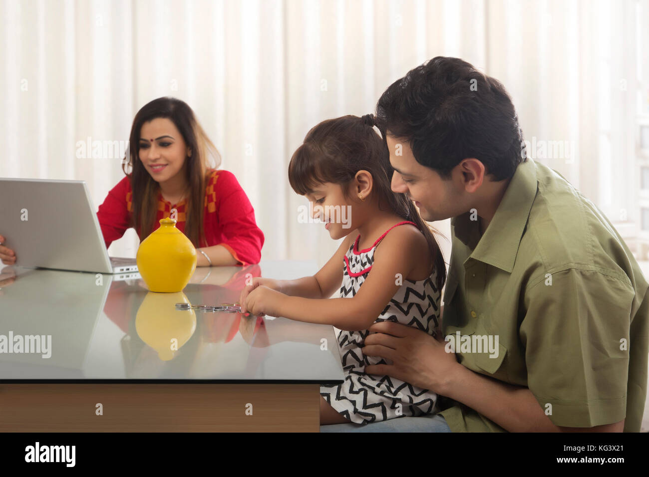 Père et fille tirelire comptage de pièces et la mère working on laptop Banque D'Images