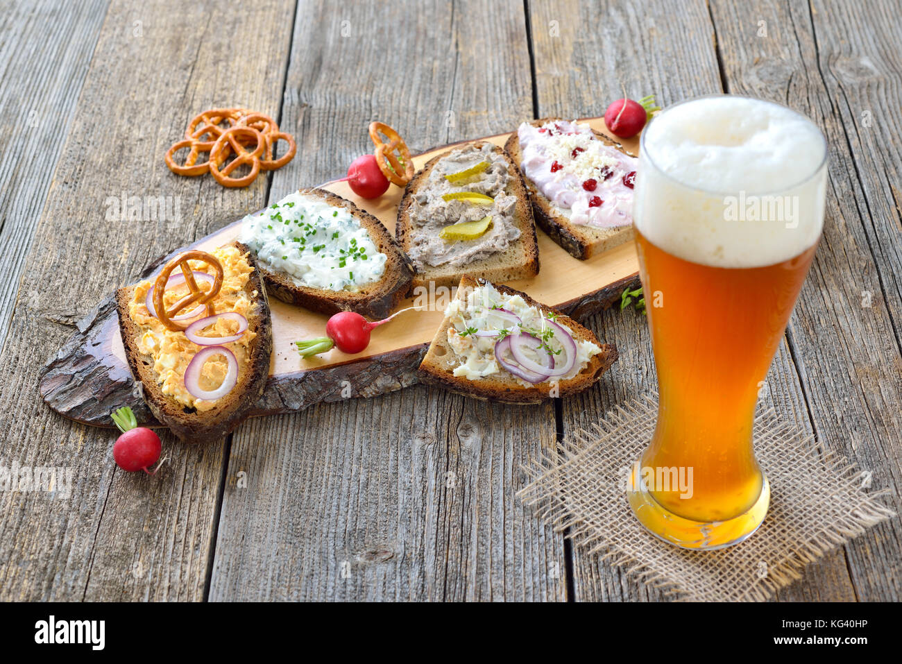 Petit snack avec différents types de pâtes à tartiner sur pain de campagne servi avec une bière de blé levure fraîche sur une vieille table en bois Banque D'Images