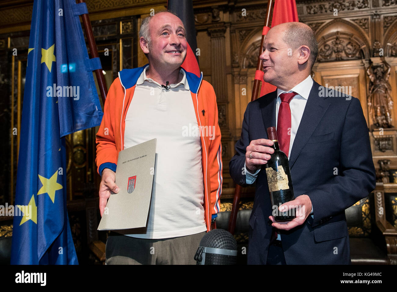 L'artiste de cabaret, Emmanuel peterfalvi (l), présente une bouteille de vin rouge pour le premier maire de Hambourg d'Olaf Scholz le parti social-démocrate d'Allemagne (SPD) après la 42e cérémonie de naturalisation dans le grand hall de l'hôtel de ville de Hambourg le 03 novembre 2017. Le comédien de paris connu sous le nom de alfons a obtenu la citoyenneté allemande vendredi. plus de 100 autochtones de Hambourg ont célébré leur naturalisation à l'hôtel de ville cérémonie. photo : christian charisius/dpa Banque D'Images