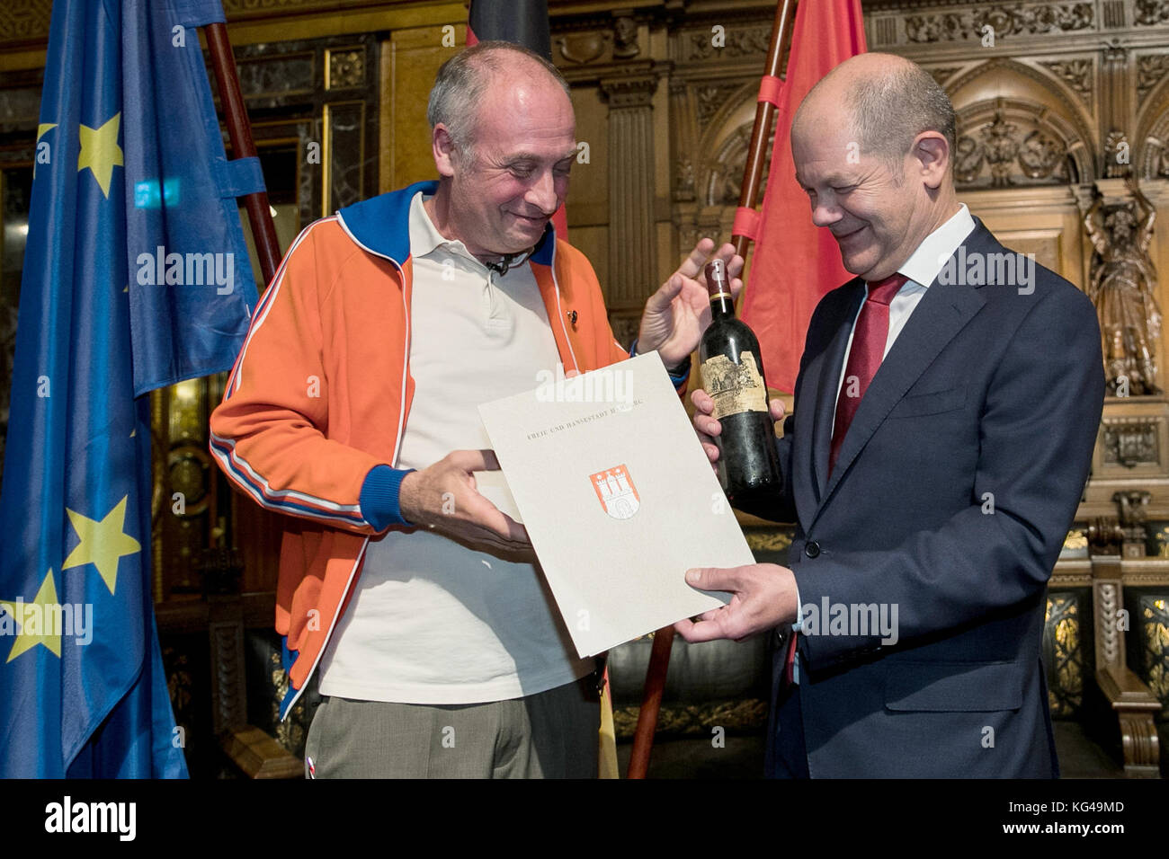 L'artiste de cabaret, Emmanuel peterfalvi (l), présente une bouteille de vin rouge pour le premier maire de Hambourg d'Olaf Scholz le parti social-démocrate d'Allemagne (SPD) après la 42e cérémonie de naturalisation dans le grand hall de l'hôtel de ville de Hambourg le 03 novembre 2017. Le comédien de paris connu sous le nom de alfons a obtenu la citoyenneté allemande vendredi. plus de 100 autochtones de Hambourg ont célébré leur naturalisation à l'hôtel de ville cérémonie. photo : christian charisius/dpa Banque D'Images
