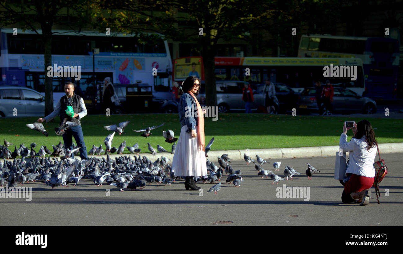 Les touristes prendre des autoportraits car les pigeons nourris par un étranger à george square Glasgow Banque D'Images