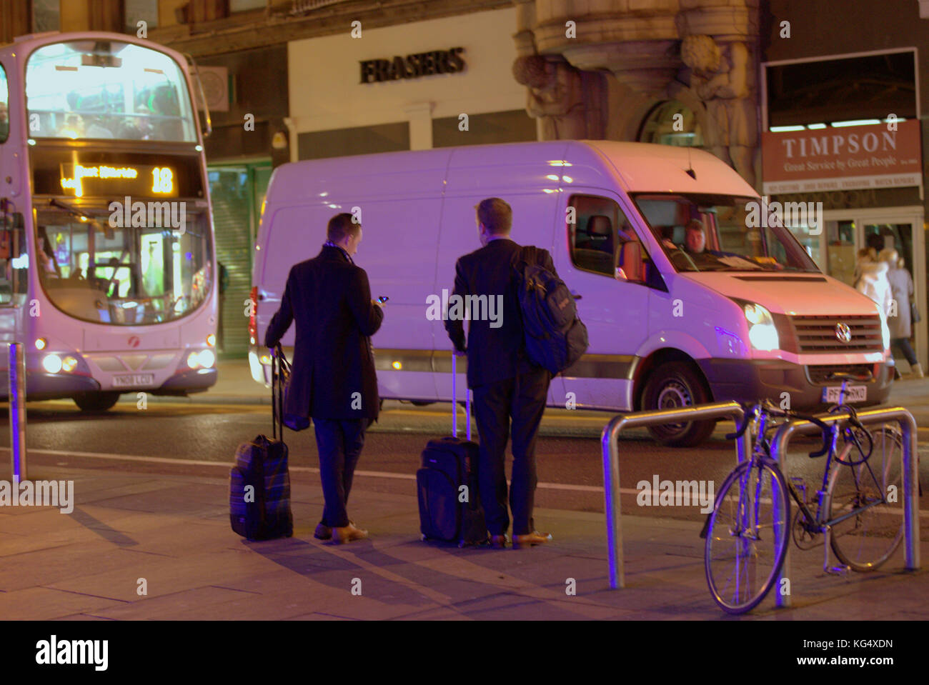 Les touristes d'affaires sur rue animée avec chariot sacs de cas en attente de uber taxi ride sur mobile smartphone vu de derrière Banque D'Images