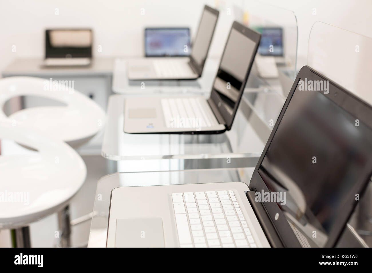 Nouveau, Ouvrir des ordinateurs portables, sur un bureau moderne en verre ; des chaises blanches en arrière-plan. Banque D'Images