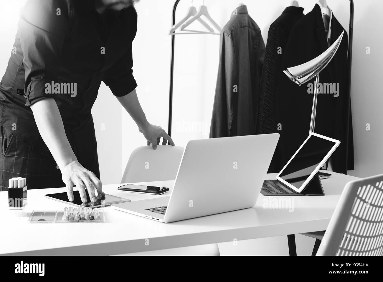 Designer de mode parle téléphone mobile et ordinateur portable avec l'aide de l'ordinateur tablette numérique en studio moderne noir et blanc, Banque D'Images