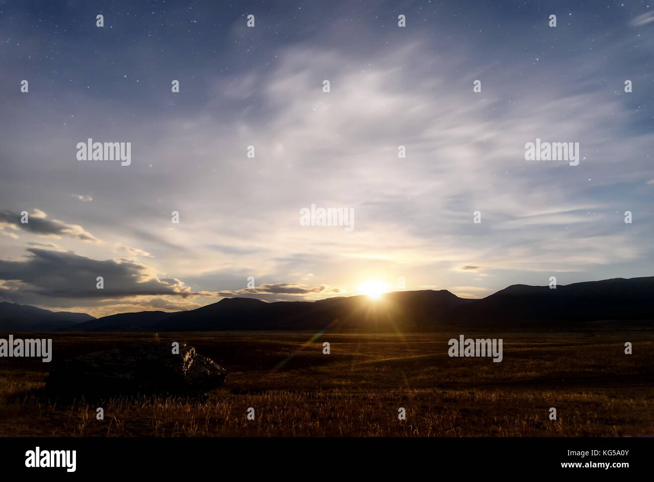 Beau paysage de nuit avec une grosse pierre dans la steppe, les phases, les étoiles et les nuages dans le ciel de nuit contre l'arrière-plan des montagnes Banque D'Images