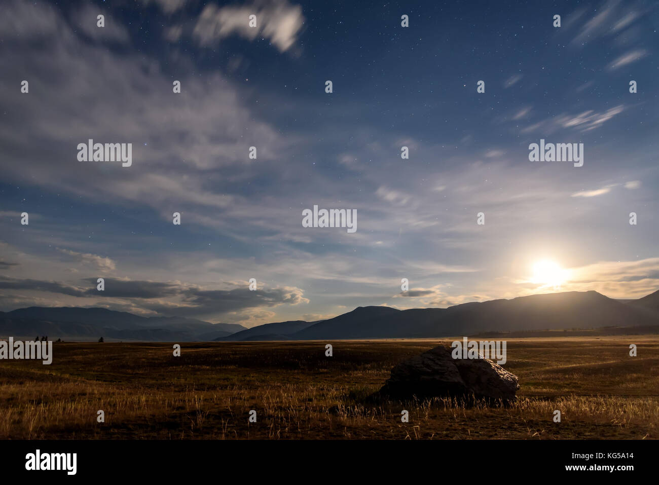 Beau paysage de nuit avec une grosse pierre dans la steppe, les phases, les étoiles et les nuages dans le ciel de nuit contre l'arrière-plan des montagnes Banque D'Images